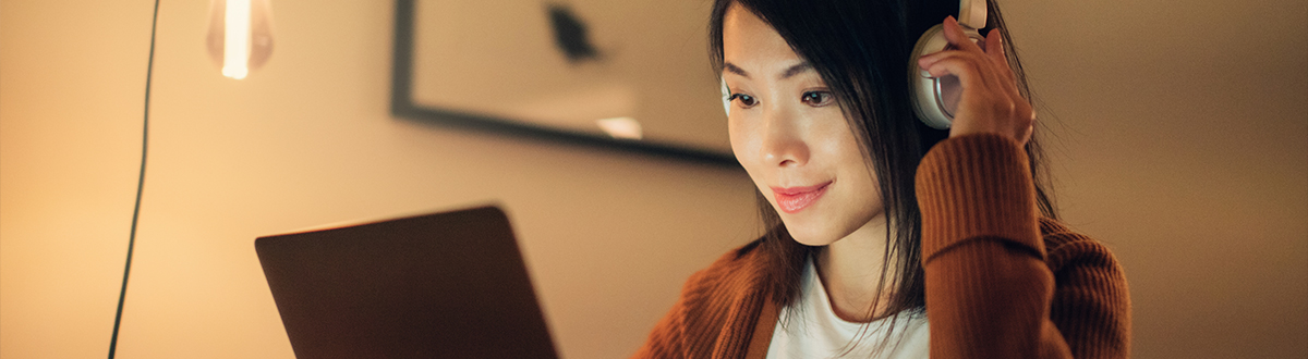 Woman wearing headphones and is on her laptop researching audience measurement solutions relevant to audio measurement.